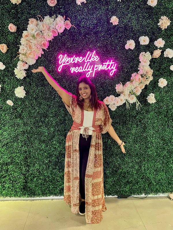 Rachana standing in front of a flower wall with neon sign